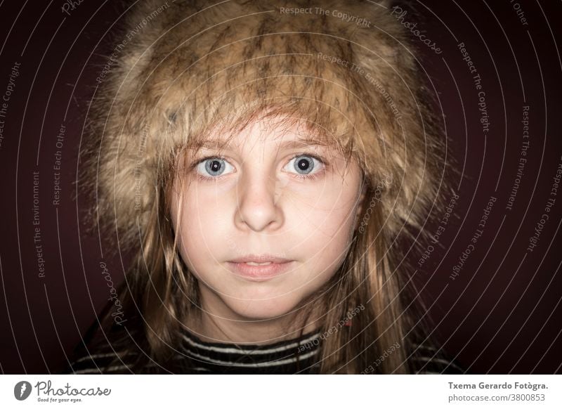 Studioporträt eines süßen Mädchens mit langen blonden Haaren, das einen Winterhut vor braunem Hintergrund trägt hübsches Mädchen Atelier-Portrait Hut Europäer