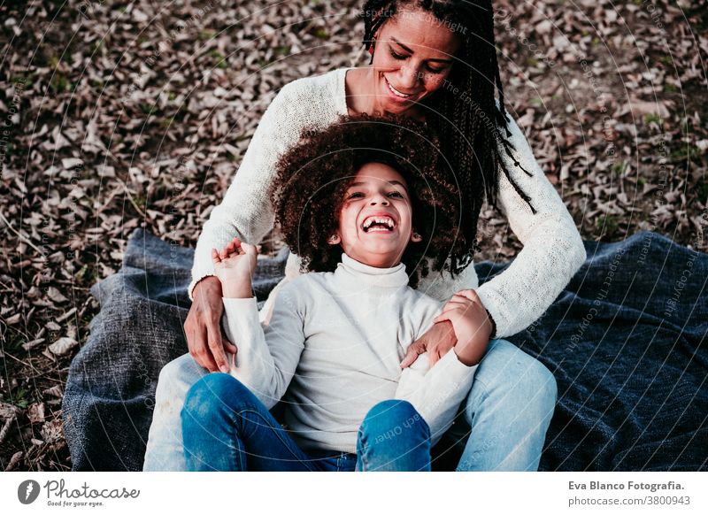 hispanische Mutter und Afrokindermädchen spielen im Freien und entspannen sich in der Natur. Herbstsaison. Familienkonzept Tochter gemischte Rasse Afro-Look