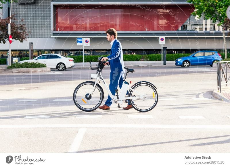 Stilvoller Mann im Anzug zu Fuß auf dem Bürgersteig mit Elektrofahrrad stylisch Bekleidung Mode elektrisch Fahrrad Spaziergang Arbeitsweg Straße maskulin formal