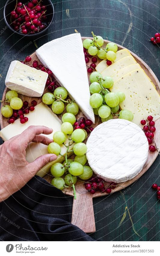 Crop gesichtslose Person dekorieren Käseplatte mit Trauben Platte Johannisbeere Speise Dessert lecker vorbereiten Küche appetitlich Küchenchef dienen Spielfigur