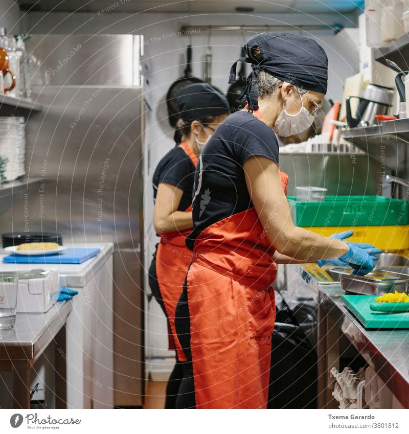 Köche in einem Restaurant, das durch eine Maske geschützt ist, als Vorsichtsmaßnahme gegen das Coronavirus, das Essen zum Mitnehmen zubereitet. Koch Küche