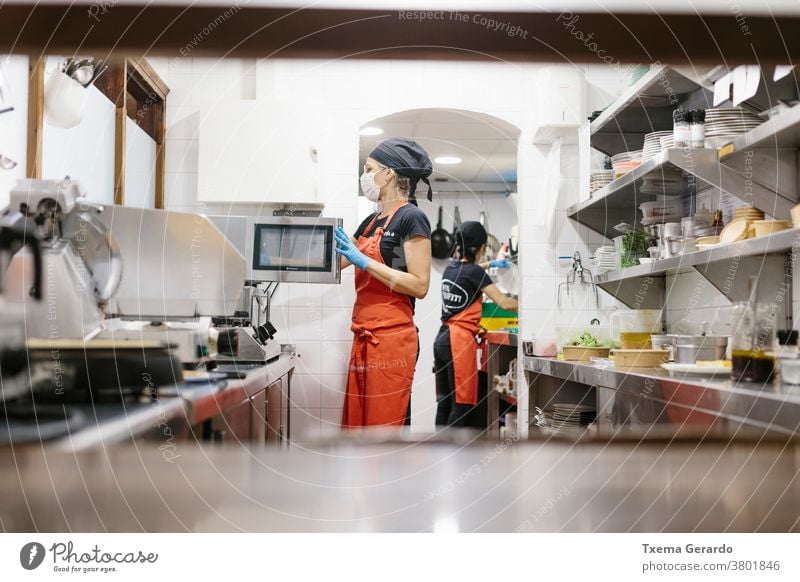 Köche in einem Restaurant, das durch eine Maske geschützt ist, als Vorsichtsmaßnahme gegen das Coronavirus, das Essen zum Mitnehmen zubereitet. Die verwendeten Behälter sind kompostierbar.