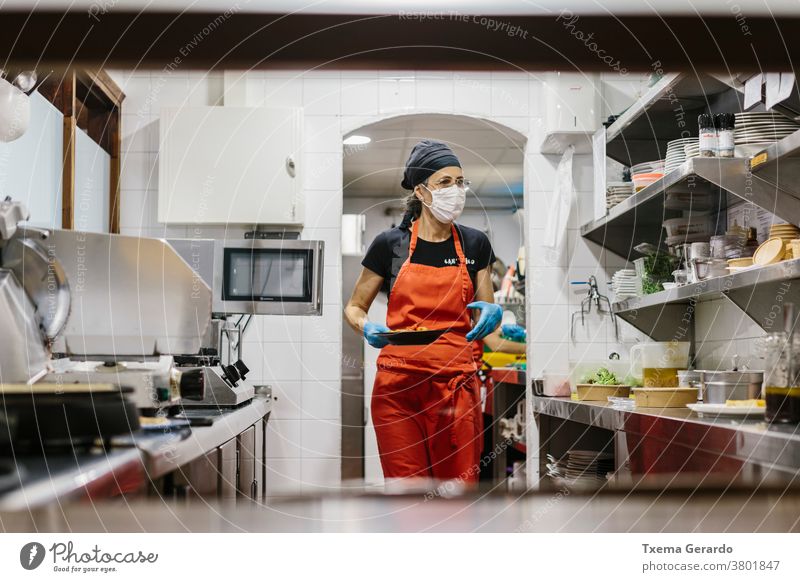 Köche in einem Restaurant, das durch eine Maske geschützt ist, als Vorsichtsmaßnahme gegen das Coronavirus, das Essen zum Mitnehmen zubereitet. Die verwendeten Behälter sind kompostierbar.