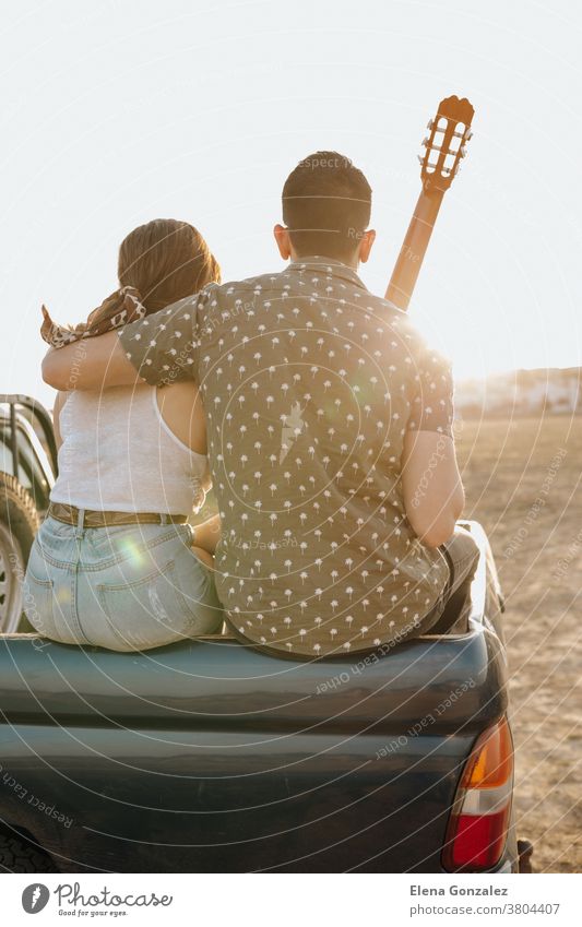 Rückansicht von jungen Reiseliebhabern, die sich mit der Gitarre auf dem Jeep 4x4-Auto vergnügen. Ein Paar macht bei Sonnenuntergang Fernweh-Urlaub Menschen