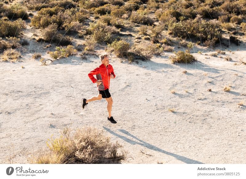 Sportler beim Joggen auf sandigem Untergrund in bergigem Gelände Mann laufen Halbwüste Hügel Training aktiv Jogger Gesundheit Natur Wohlbefinden Sand Übung