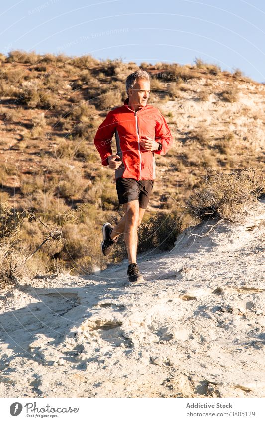 Sportler beim Joggen auf sandigem Untergrund in bergigem Gelände Mann laufen Halbwüste Hügel Training aktiv Jogger Gesundheit Natur Wohlbefinden Sand Übung