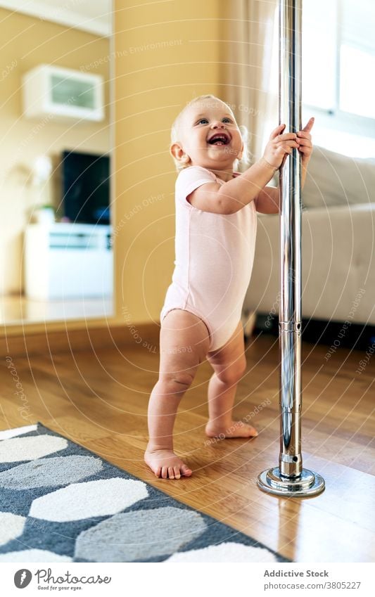 Nettes Baby auf dem Boden stehend und lachend heiter Lachen Mast heimwärts Glück Freude Schritt Kindheit positiv froh Tageslicht Säugling Mädchen Body blond