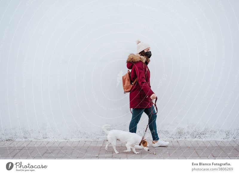 Frau mit Schutzmaske, die mit ihrem liebenswerten Hund Jack Russell durch die Stadt spaziert. Lebensstil im Freien Erwachsener allergisch Herbst Hintergrund