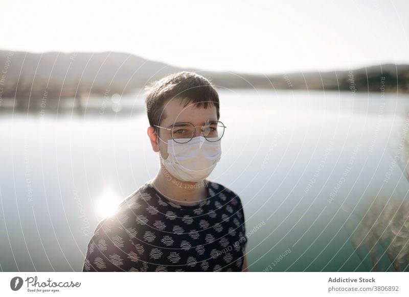 Anonymer männlicher Reisender in Maske und Brille in der Nähe eines Sees Mundschutz Natur Berge u. Gebirge Himmel Sonnenschein Mann Bund 19 reisen Sommer