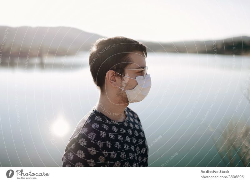 Männlicher Reisender in Maske und Brille in der Nähe von See Mundschutz Natur Berge u. Gebirge Himmel Sonnenschein Mann Bund 19 reisen Sommer Reittier Tourismus