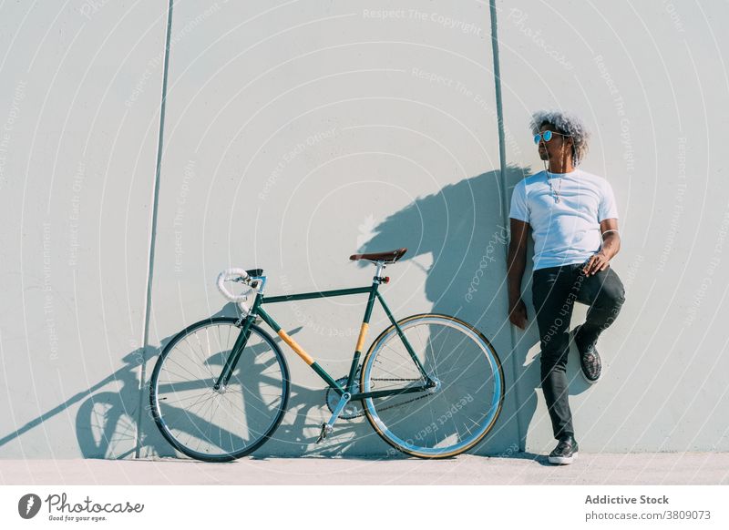 Schwarzer Radfahrer, der neben seinem Stadtrad an einer grauen Wand lehnt. schwarzer Radfahrer Reiter Schwarzer Reiter Fahrrad Afro-Look Schwarzer Mann