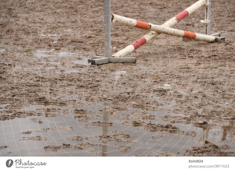 Pferdesportplatz mit gekreuztem Hindernis versinkt im Matsch mit Pfütze Springreiten Hindernisreiten Schlamm überflutet Ständer rot-weiß BArriere Hürde Palisade