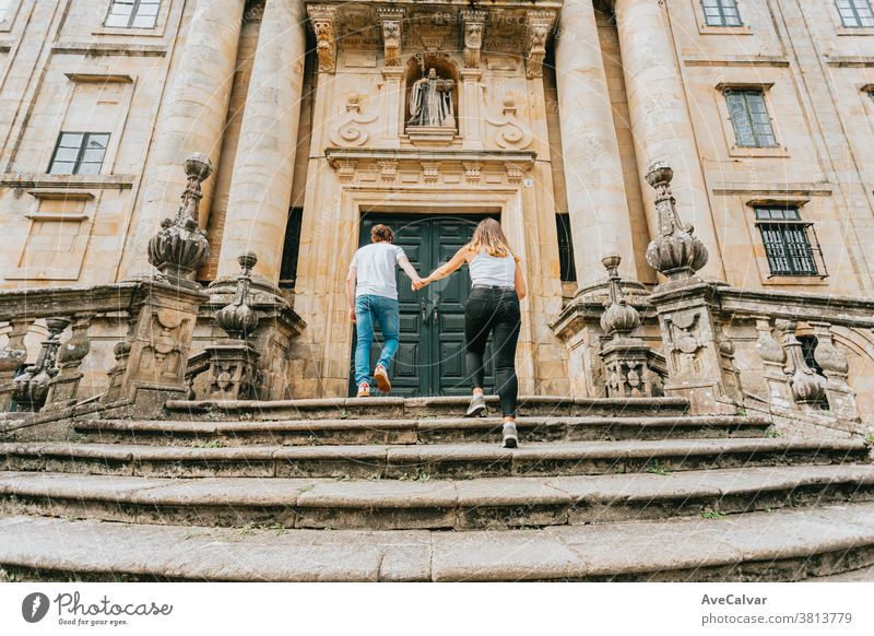 Junges Paar geht an einem sonnigen Tag in einem alten Gebäude eine Treppe hinauf und fasst sich an den Händen außerhalb Urlauber Mann Treppenhaus im Freien