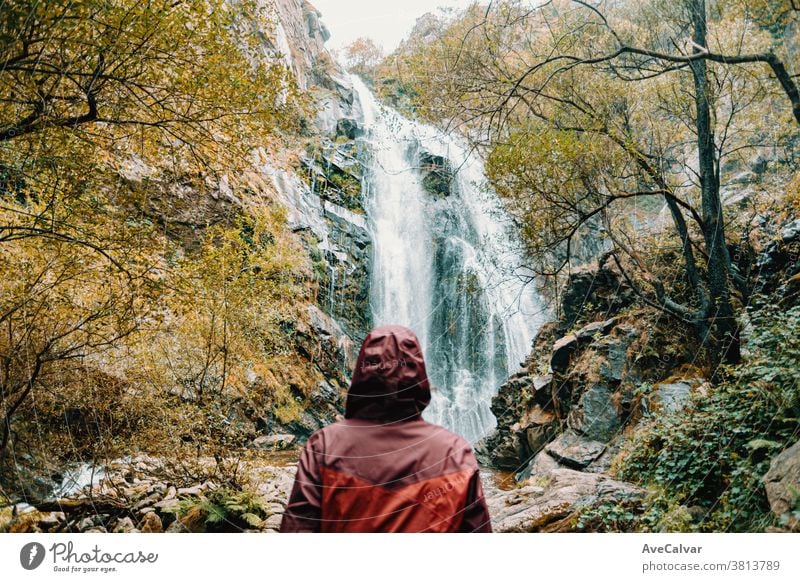 Unscharfe Frau in violettem Ölzeug steht vor einem riesigen Wasserfall Rucksack im Freien Wald Menschen Blick Ansicht weiß Abenteuer sonnig erkundend genießen