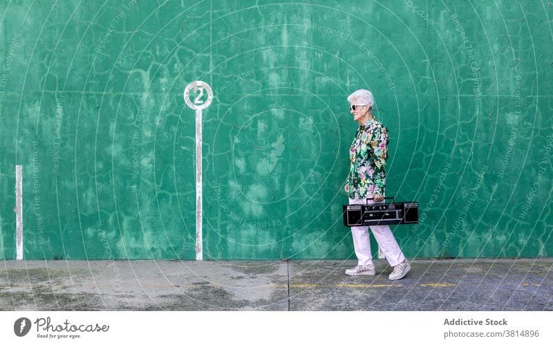 Ältere Frau mit Plattenspieler in der Nähe der Wand stehend Senior Spieler Musik Stil älter zuhören Klang aktiv Aufzeichnen trendy Lifestyle urban gealtert