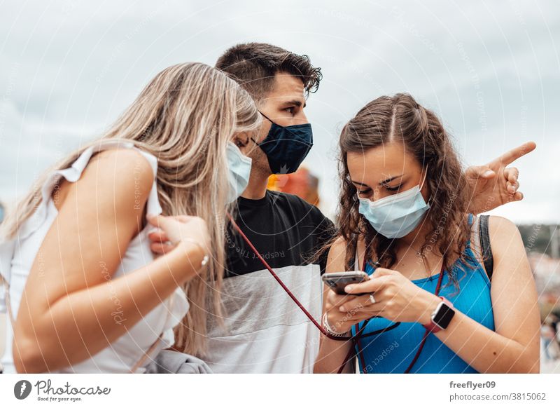 Gruppe von Freunden mit chirurgischen Masken, die auf einem Smartphone suchen Orientierung Menschengruppe Kaukasier zwanglose Kleidung durchsuchend Telefon