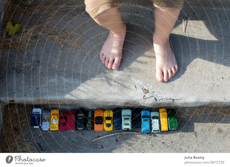 Spielzeugautos in einer Reihe auf Betontreppen in der Nähe von Kinderfüßen; Spiel im Freien Spielen spielerisch Fuß Zehen Linie aufgereiht freies Spiel offen