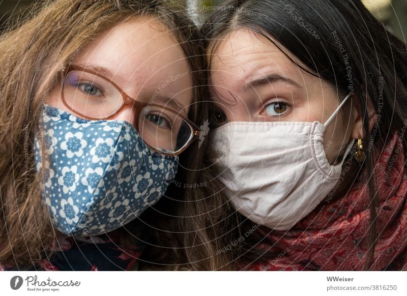 Zwei Mädchen tragen Masken und schauen skeptisch in die Kamera Junge Frauen zur gleichen Zeit Nähe Blick zwei Frauen 2 Menschen verspielt unsicher spektakulär