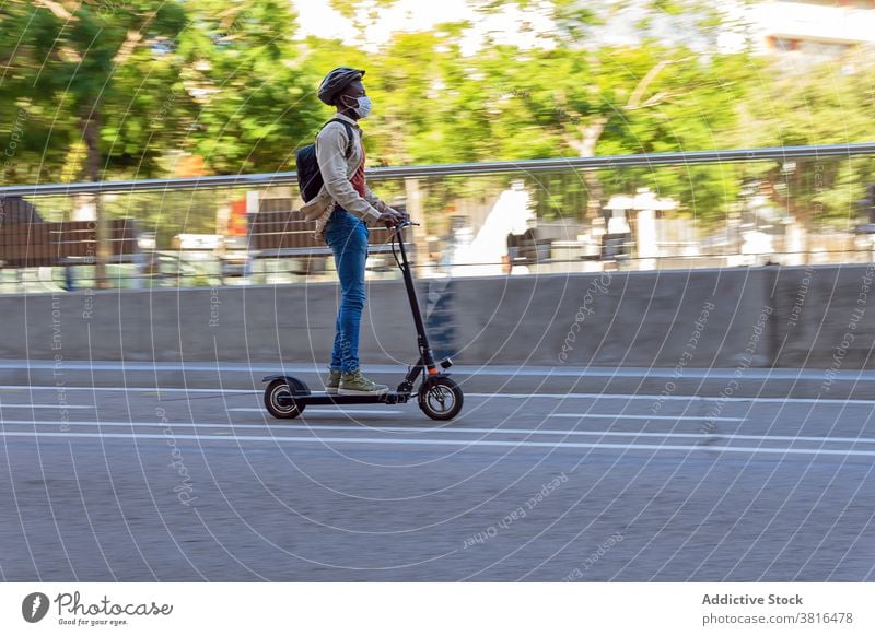 Ethnischer Mann fährt mit Elektroroller über den Zebrastreifen Arbeitsweg Tretroller Mitfahrgelegenheit Großstadt elektrisch Sommer Straße Mundschutz männlich