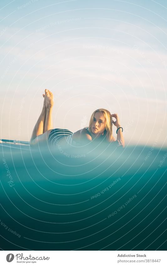 Gelassene Frau auf Surfbrett im Meer Lügen MEER sich[Akk] entspannen Sonnenuntergang schlank Badeanzug Wasser winken Himmel Erholung Sommer Badebekleidung ruhen