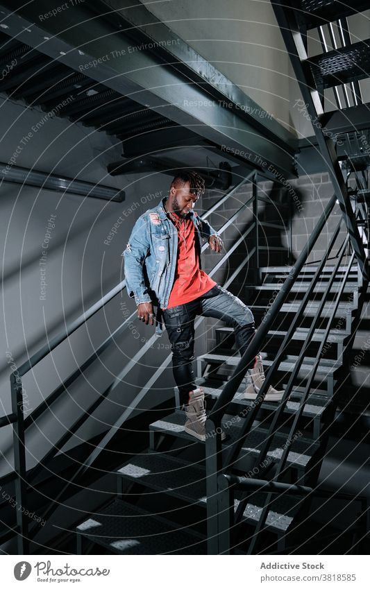 Schwarzer Mann in stilvoller Kleidung auf Metalltreppe trendy Bekleidung Jeansstoff Jacke Streetstyle Stil Mode nachdenklich Vorschein männlich ethnisch schwarz