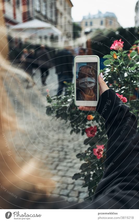 Junge Frau mit Videogesprächen, die abends auf einem Spaziergang durch die Innenstadt mit der Gesichtsmaske spricht, um eine Virusinfektion zu vermeiden Anruf