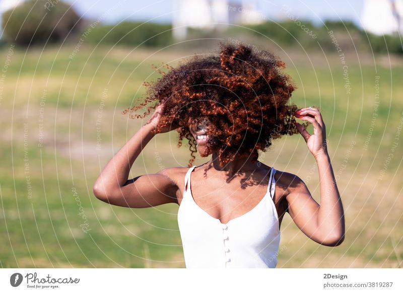 Schöne afroamerikanische Frau in weißem Kleid, die an einem sonnigen Tag im Gras in einem Park sitzt. Sitzen Afro-Look 1 Afroamerikaner jung Porträt im Freien