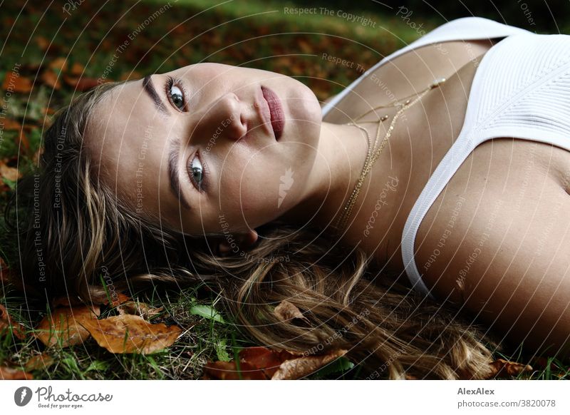 Seitliches Portrait eines Mädchen in weißem Trägertop das auf einer Herbstwiese mit Laub liegt Landschaft Strand intensiv jugendlich freundlich Natur weiblich