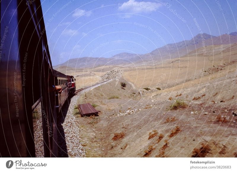 Blick aus fahrendem Zug in eine trockene bergige Landschaft zug Zugfahrt alt retro Wüste Steppe heiß Süden Ferne Weite Bahnfahren unterwegs sein Tour Reise