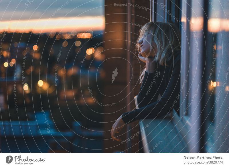 Porträt einer kaukasischen Frau, die zur blauen Stunde am Fenster lehnt. blond Sternstunde Zauberei u. Magie Farbfoto Blick Mensch Mode Lifestyle Stil Bokeh