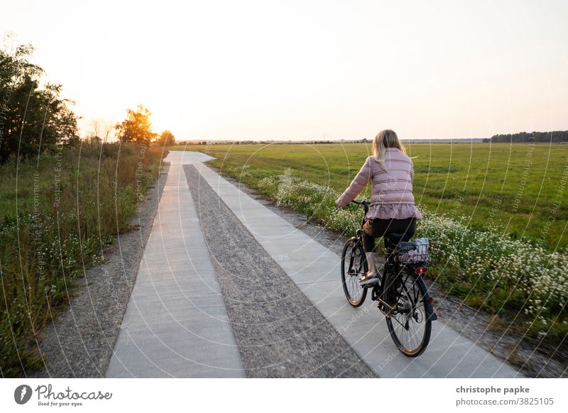 Frau fährt Fahrrad im Sonnenuntergang Fahrradfahren Feld Fahrradtour Wege & Pfade Bewegung Mobilität Ausflug Freizeit & Hobby blond Außenaufnahme Farbfoto