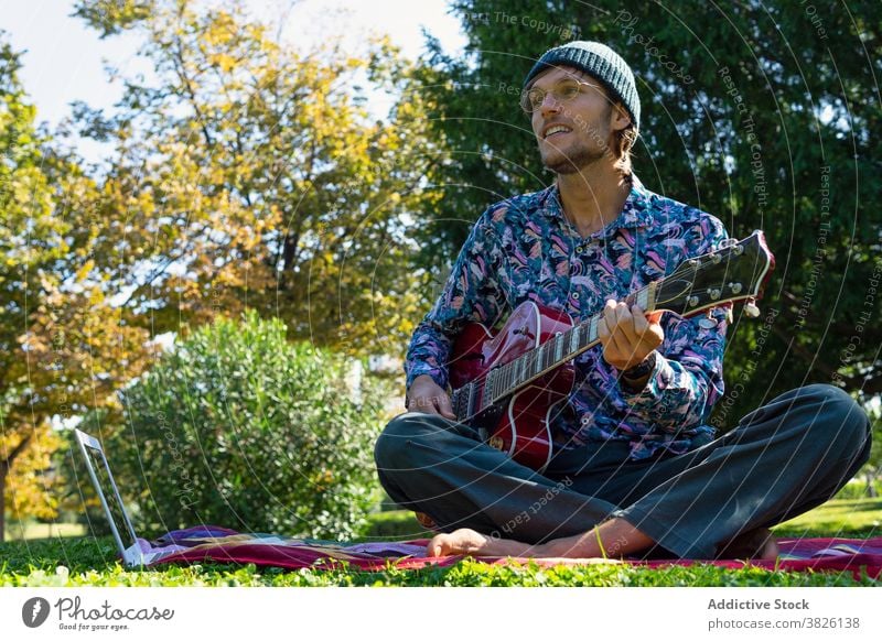 Mann mit E-Gitarre im Park elektrisch Tutorial Laptop Gitarrenspieler Spieler Lektion Musik spielen männlich Musiker Decke Klang Melodie Gesang Hobby modern