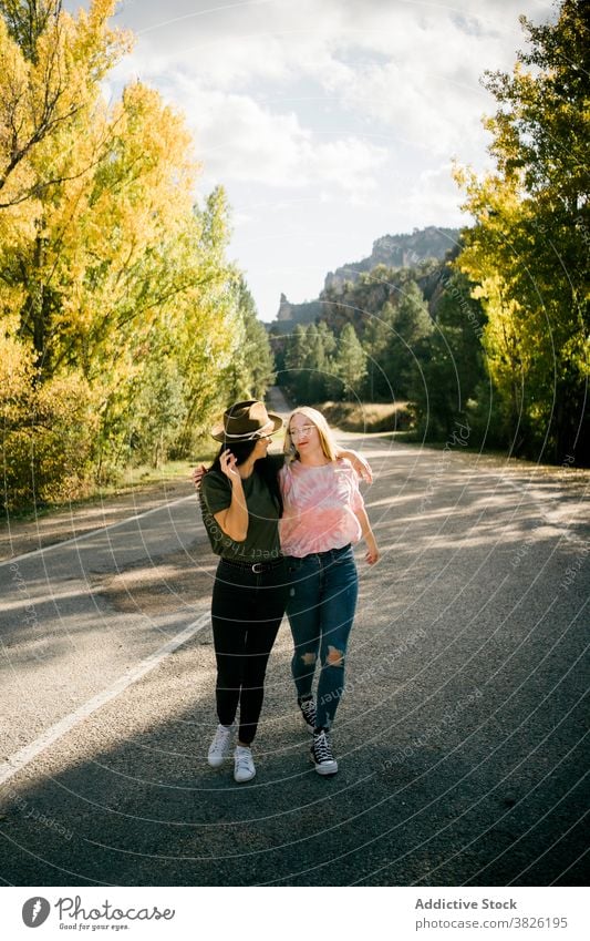 Glückliche Freundinnen umarmen sich auf der Landstraße Frauen Straße Wald Umarmung Herbst Freundschaft Landschaft Natur heiter jung Fahrbahn Zusammensein