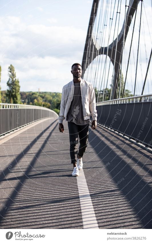 Junger schwarzer Mann geht selbstbewusst auf der Brücke afrikanische ethnische Zugehörigkeit Spaziergang echte Person eine Person Nur ein Mann modisch