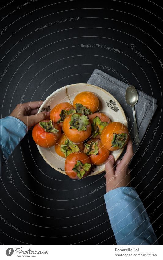 Teller Kakipflaume und Hände Herbst biologisches schwarzer Hintergrund Textfreiraum dunkel lecker Lebensmittel Früchte gut Gesundheit Beteiligung