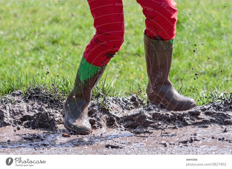 Beine in roter Hose und grünen Gummistiefel springen in einer matschigen Pfütze, so dass der Matsch hochfliegt matschen fliegen Sprung Schlamm spritzen Stiefel