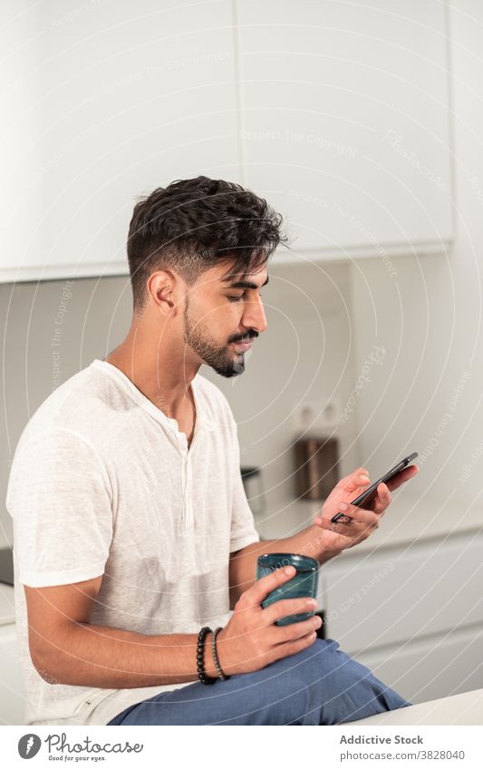 Ernster Mann beim Frühstück in der Küche Morgen Kaffee Smartphone früh heimwärts Browsen Tasse männlich heimisch Outfit trinken Apparatur Gerät Windstille