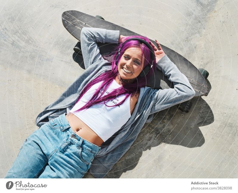 Entschlossene Frau mit Longboard in der Stadt tausendjährig unabhängig informell jung rosa Haare ausgefallen Skater selbstbewusst modern Hipster Mode trendy