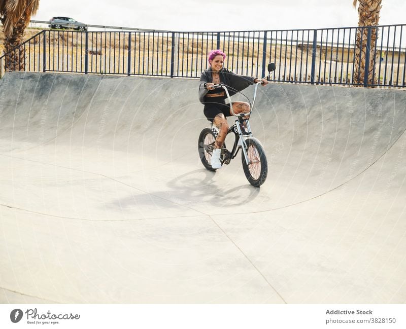 Glückliche Frau auf dem Fahrrad im Skatepark bmx selbstbewusst Skateplatz extrem Tattoo Stil Outfit sitzen trendy urban jung cool Verkehr Freiheit Sommer