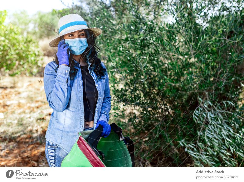 Junge Frau in medizinischer Maske, die während der Ernte auf dem Smartphone spricht Telefonanruf Mundschutz COVID Gespräch benutzend Garten reden behüten