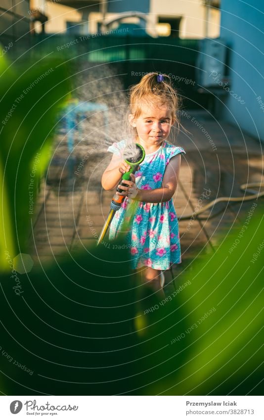 Glückliches 2-3-jähriges Mädchen mit Gartenschlauch gießt die Pflanzen. Baby Wattering Hinterhof Familie Wasser Liebe Kind Person Sommer Natur Sonne Tier