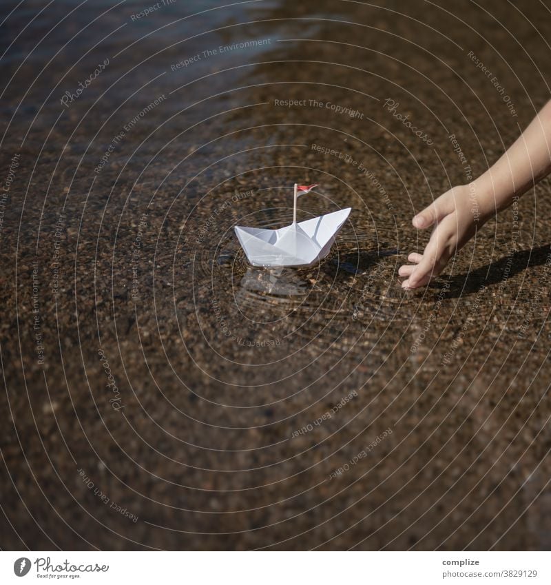 Kleines Kind setzt ein Papierschiff ins Wasser Farbfoto Lebenslauf Strand Seeufer Zukunft 3-8 Jahre Küste Wellen Kindheit Hand Güterverkehr & Logistik Schulkind