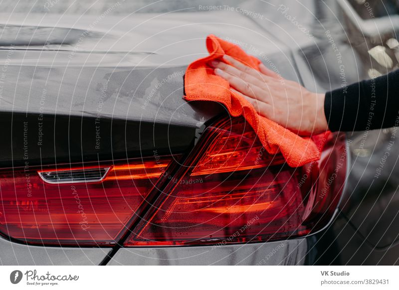 Konzept des Reinigungsautos. Mans wischt die Motorhaube mit einem Mikrofasertuch von Hand ab. Nicht erkennbarer Mann poliert Fahrzeug. Detaillierung oder Aufwertung