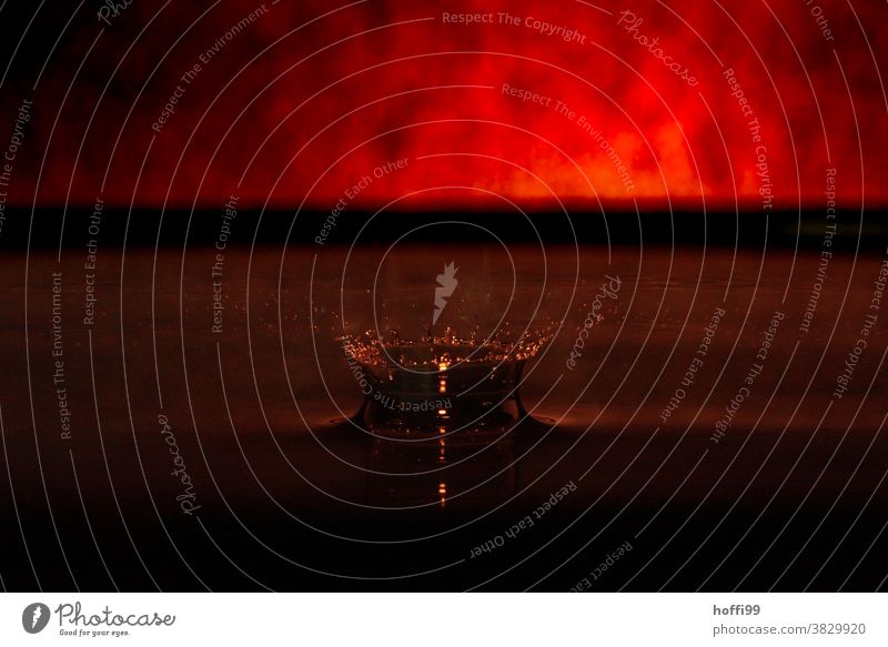 ein Tropfen fällt in ein Gefäß mit Wasser - rote Glut schimmert am Horizont roter hintergrund Blutrot feuer feuerrot tropfenbild Makroaufnahme Farbe nass