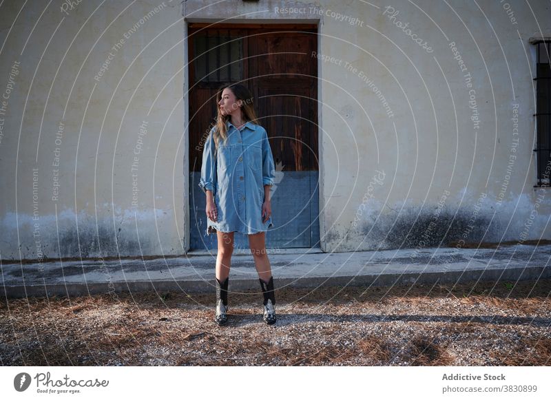 Stilvolle junge Frau steht in der Nähe von schäbigen Gebäude Jeansstoff Kleid Landschaft Herbst trendy kalt Haus schlank Raureif verwittert ländlich Saison