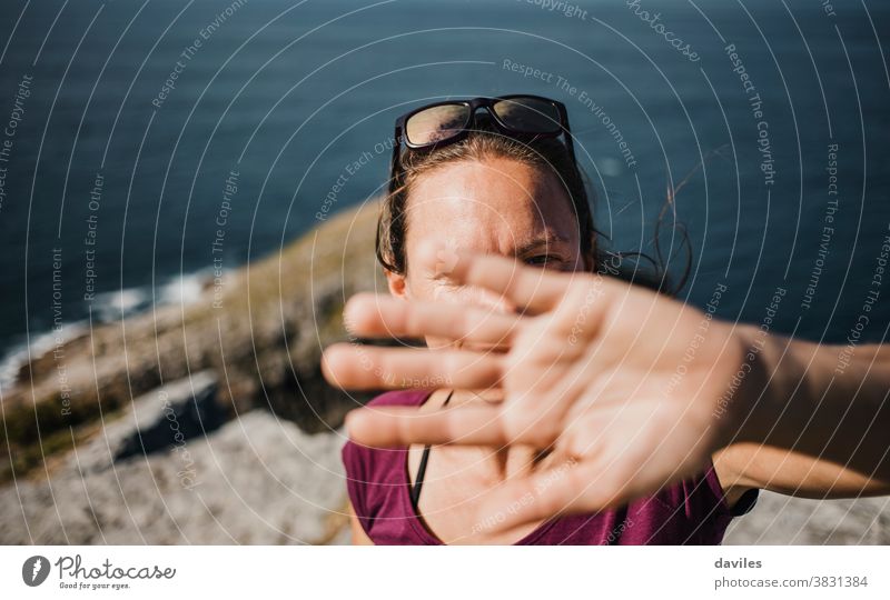 Verspielte Frau, die versucht, sich vor der Kamera des Fotografen zu verstecken, um Bilder zu vermeiden. Berge u. Gebirge MEER Natur Küste im Freien Arme Hand