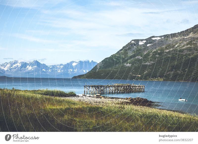 Fjordlandschaft in Norwegen mit einem Steg der ins Wasser führt, dem Blick auf den Fjord und Schneebedeckten Bergen im Hintergrund. Fjordausblick Landschaft