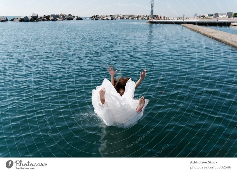 Anonyme Frau im Brautkleid fällt ins Wasser weißes Kleid hochzeitlich fallen Barfuß Strandpromenade See Pier jung aufgeregt ertrinken Spaß flippig Stauanlage