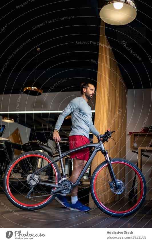 Sportler mit Fahrrad in der Turnhalle Fitnessstudio Spaziergang Training vorbereiten modern Sportbekleidung männlich Athlet passen Aktivität Ausdauer Kraft