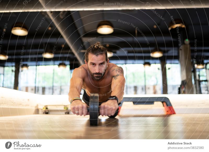 Bärtiger Sportler beim Training mit Abs-Rad Übung Fitnessstudio Bauchmuskeln Stock modern ohne Hemd stark männlich Athlet Erwachsener physisch Stärke anstrengen